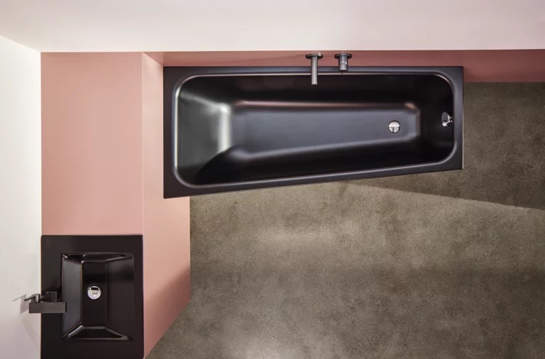 Baignoire asymétrique noire Bette Space, installée dans un angle avec mur rose et sol en béton ciré