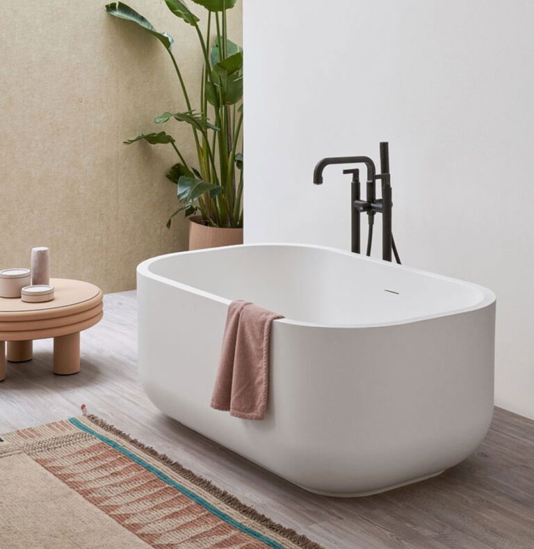 Baignoire en îlot Dafne de Cielo, posée sur un sol en bois clair avec robinetterie noire et plantes vertes