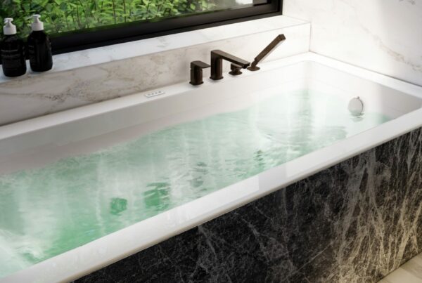 Baignoire balnéothérapie rectangulaire avec eau chaude, lumière naturelle et vue végétale, dans une salle de bains en marbre, ambiance spa à domicile.