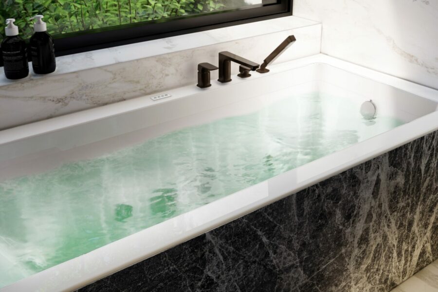 Baignoire balnéothérapie rectangulaire avec eau chaude, lumière naturelle et vue végétale, dans une salle de bains en marbre, ambiance spa à domicile.
