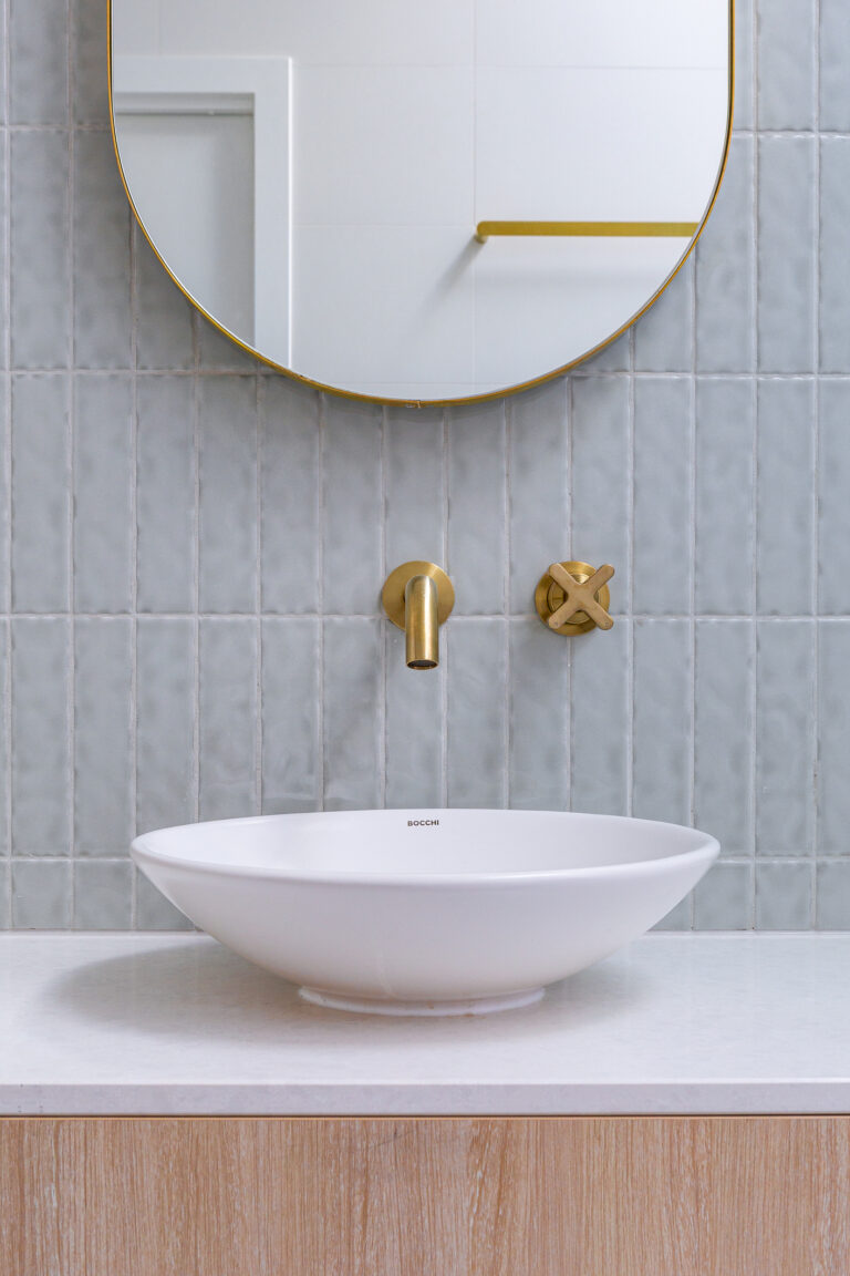 Vasque blanche sur plan en marbre devant un mur en zellige gris clair avec robinet doré mural