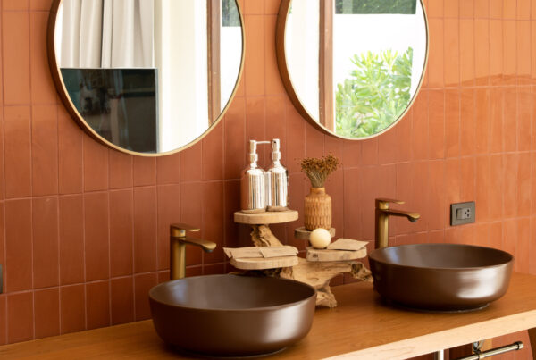 Salle de bains avec mur en zellige terracotta, deux vasques rondes marron et miroirs circulaires