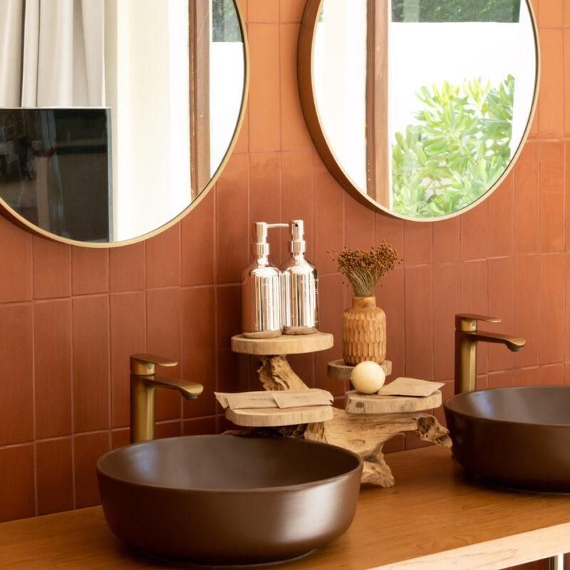 Salle de bains avec mur en zellige terracotta, deux vasques rondes marron et miroirs circulaires