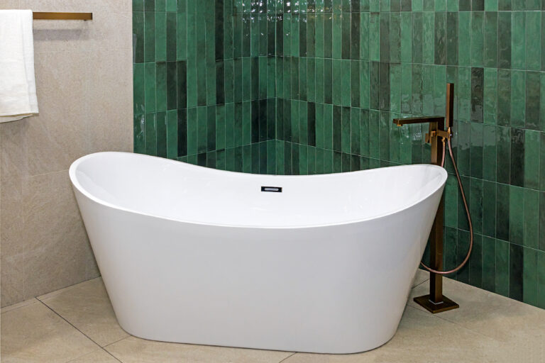 Baignoire îlot blanche devant un mur en zellige vert, avec robinetterie cuivrée au sol