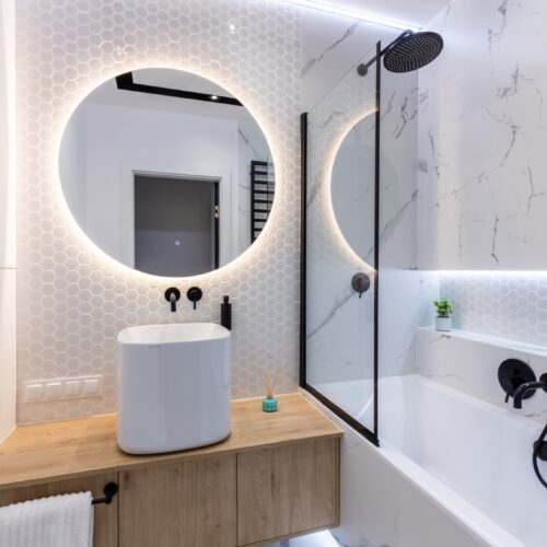 Salle de bains design avec baignoire et douche intégrées, robinetterie noire mate et miroir rétroéclairé