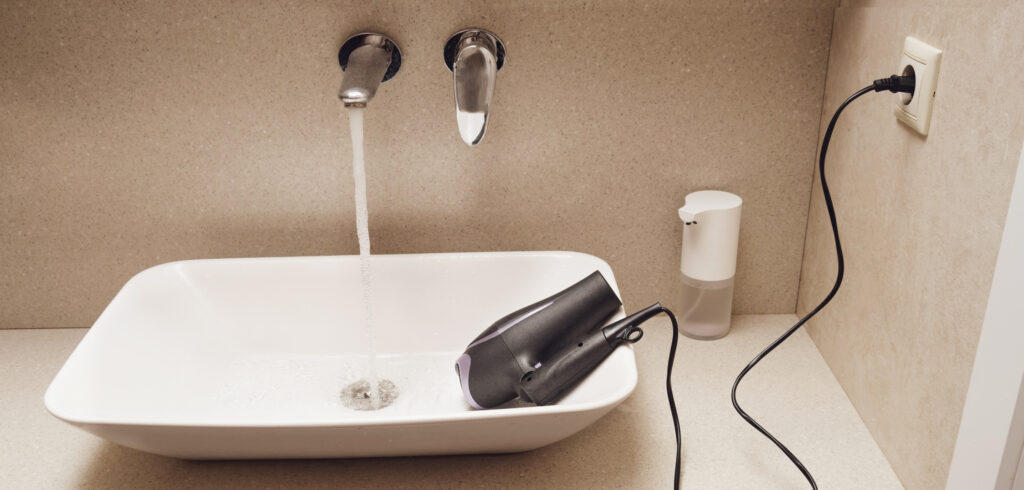 Exemple de risque électrique dans une salle de bains avec un sèche-cheveux branché posé dans un lavabo, illustration de la nécessité des normes de sécurité électrique
