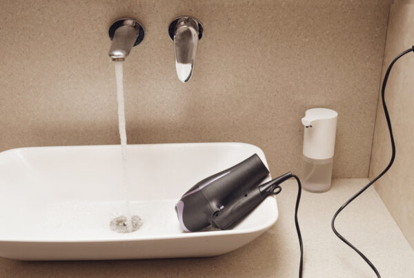 Exemple de risque électrique dans une salle de bains avec un sèche-cheveux branché posé dans un lavabo, illustration de la nécessité des normes de sécurité électrique