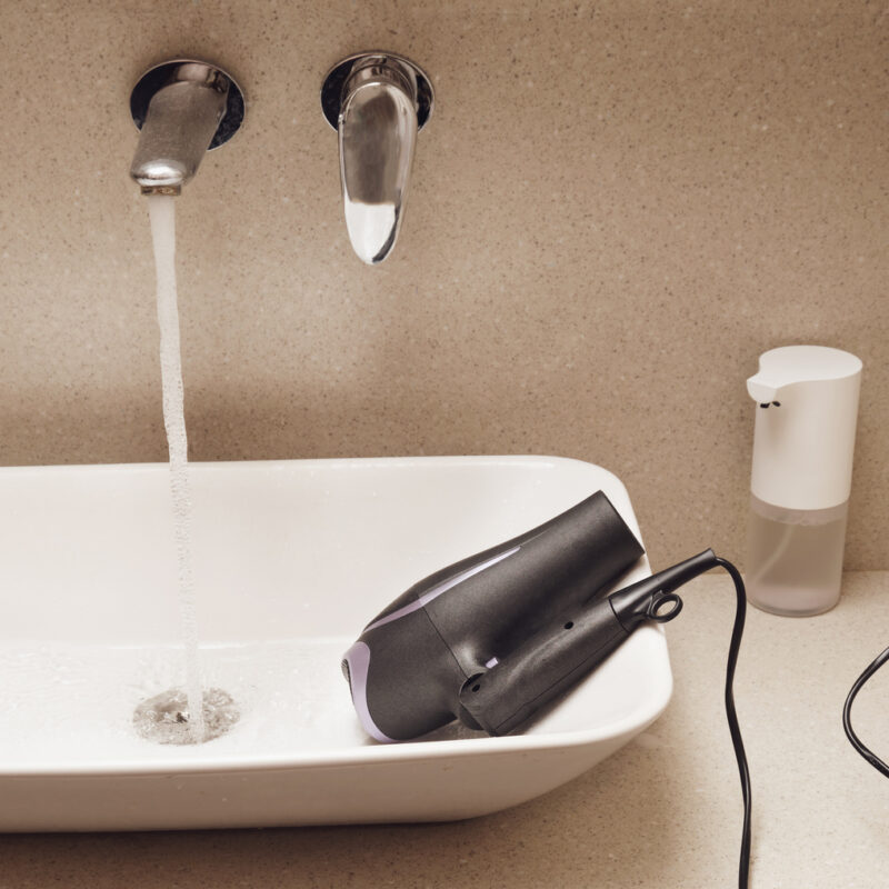 Exemple de risque électrique dans une salle de bains avec un sèche-cheveux branché posé dans un lavabo, illustration de la nécessité des normes de sécurité électrique