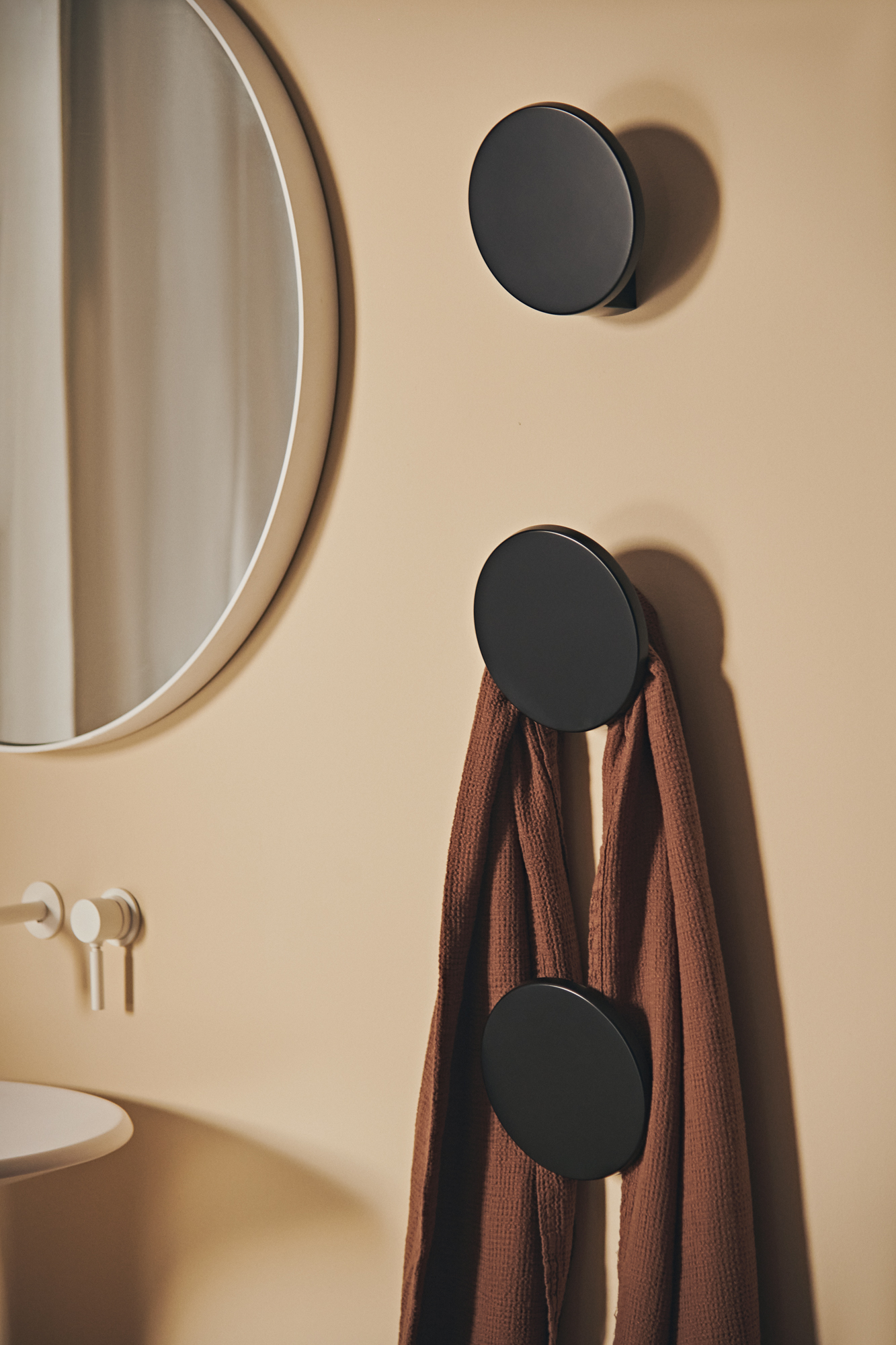 Sèche-serviettes mural noir design Dots de la marque Tubes, fixé en patères rondes sur un mur beige dans une salle de bains épurée