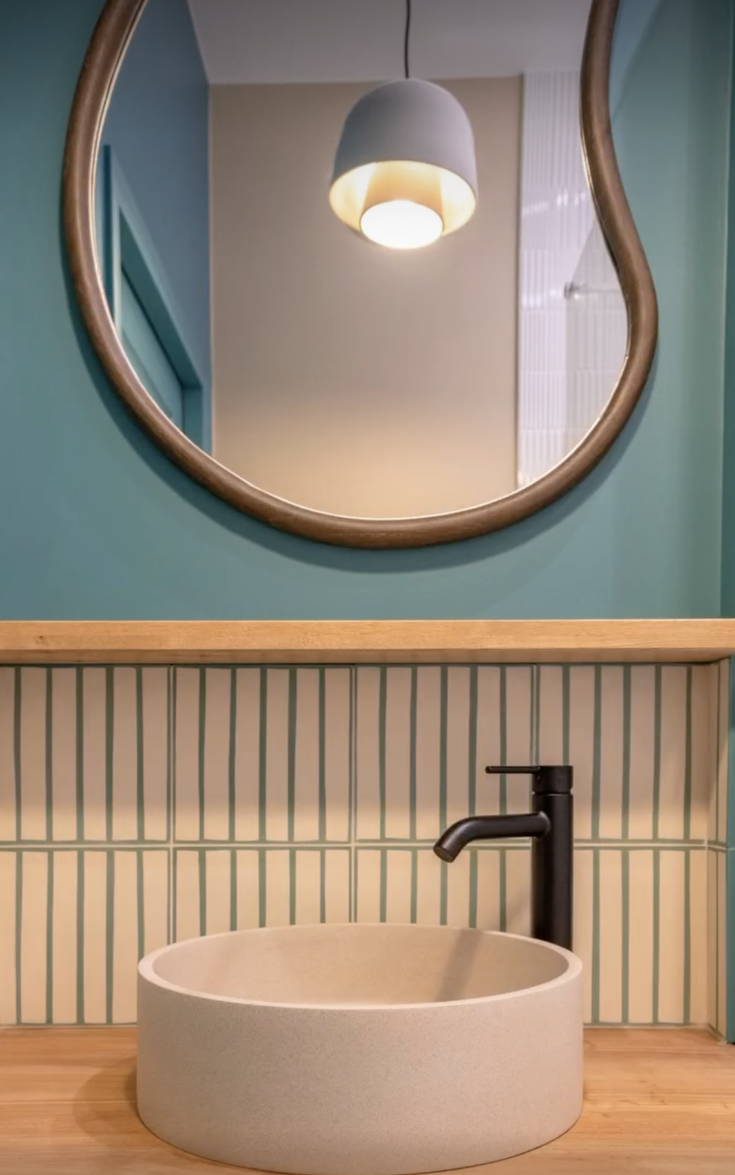 Lave-mains rond en céramique beige avec robinet noir mat, fond bleu canard et crédence en carreaux de ciment Carocim
