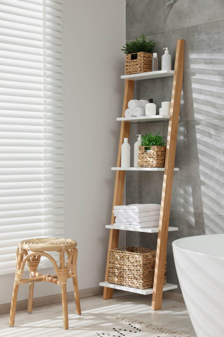 Étagère ouverte en bois et blanc avec paniers tressés, produits épurés et serviettes roulées dans une salle de bains lumineuse