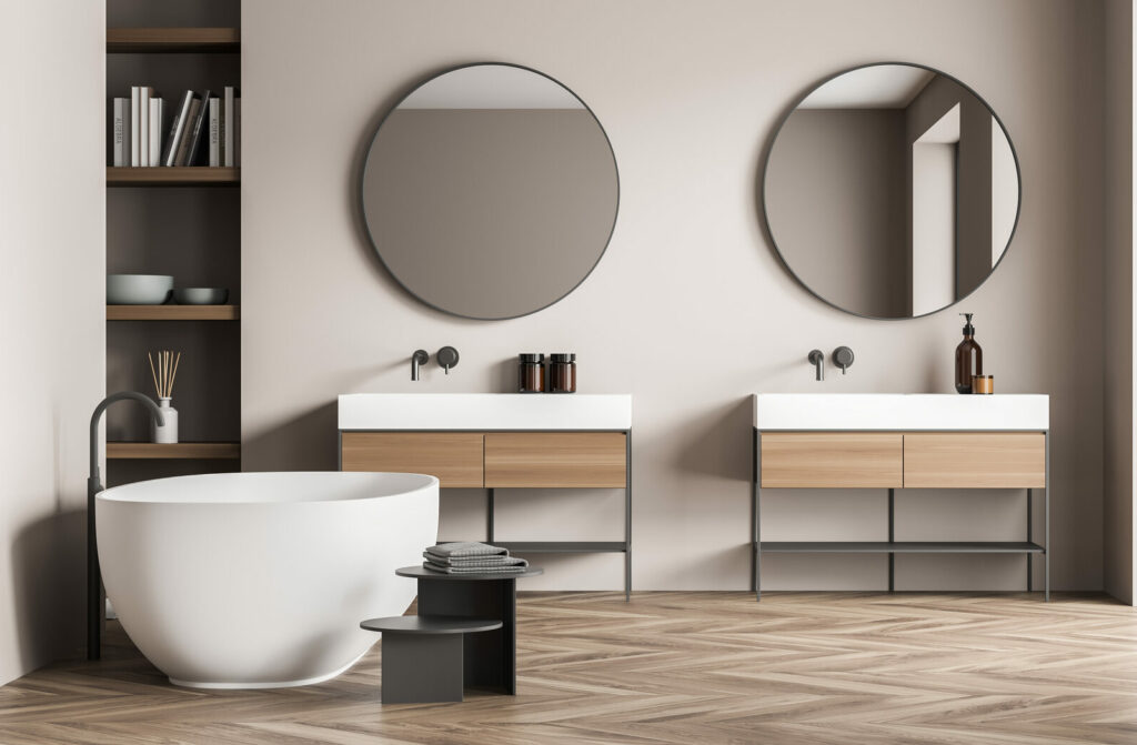 Salle de bains minimaliste aux tons beige et bois clair, avec baignoire îlot, double vasque et grande fenêtre apportant une lumière naturelle douce