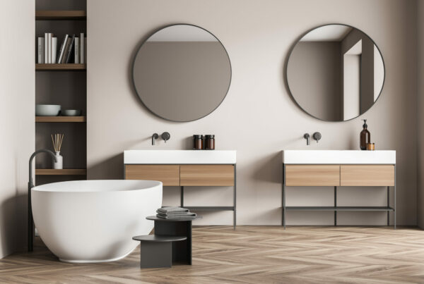 Salle de bains minimaliste aux tons beige et bois clair, avec baignoire îlot, double vasque et grande fenêtre apportant une lumière naturelle douce