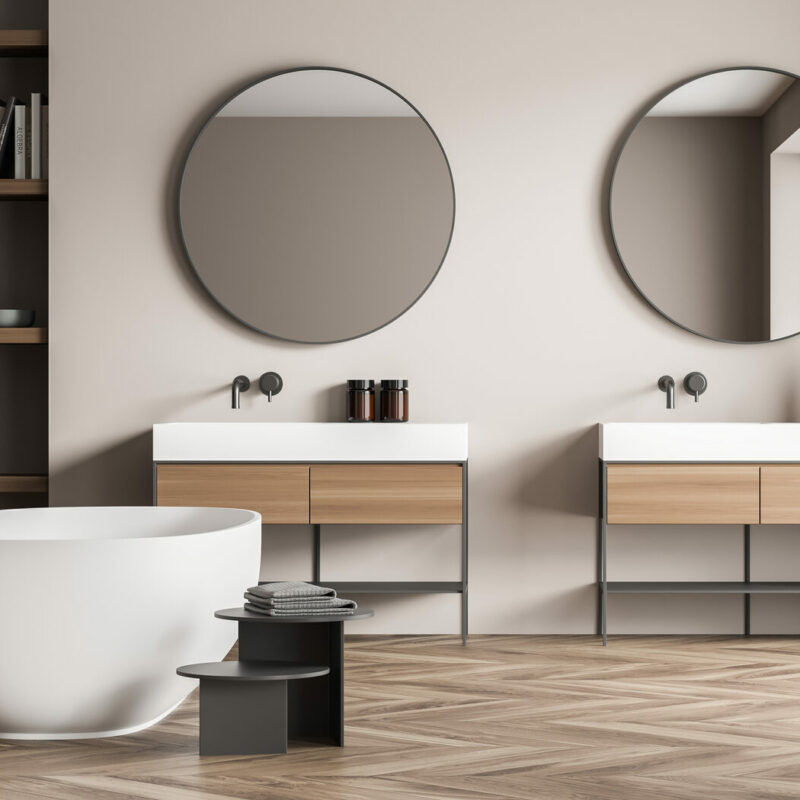 Salle de bains minimaliste aux tons beige et bois clair, avec baignoire îlot, double vasque et grande fenêtre apportant une lumière naturelle douce