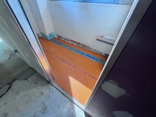 Salle de bains en cours de rénovation avec cloisons posées, murs remis en état et natte d’étanchéité orange au sol.