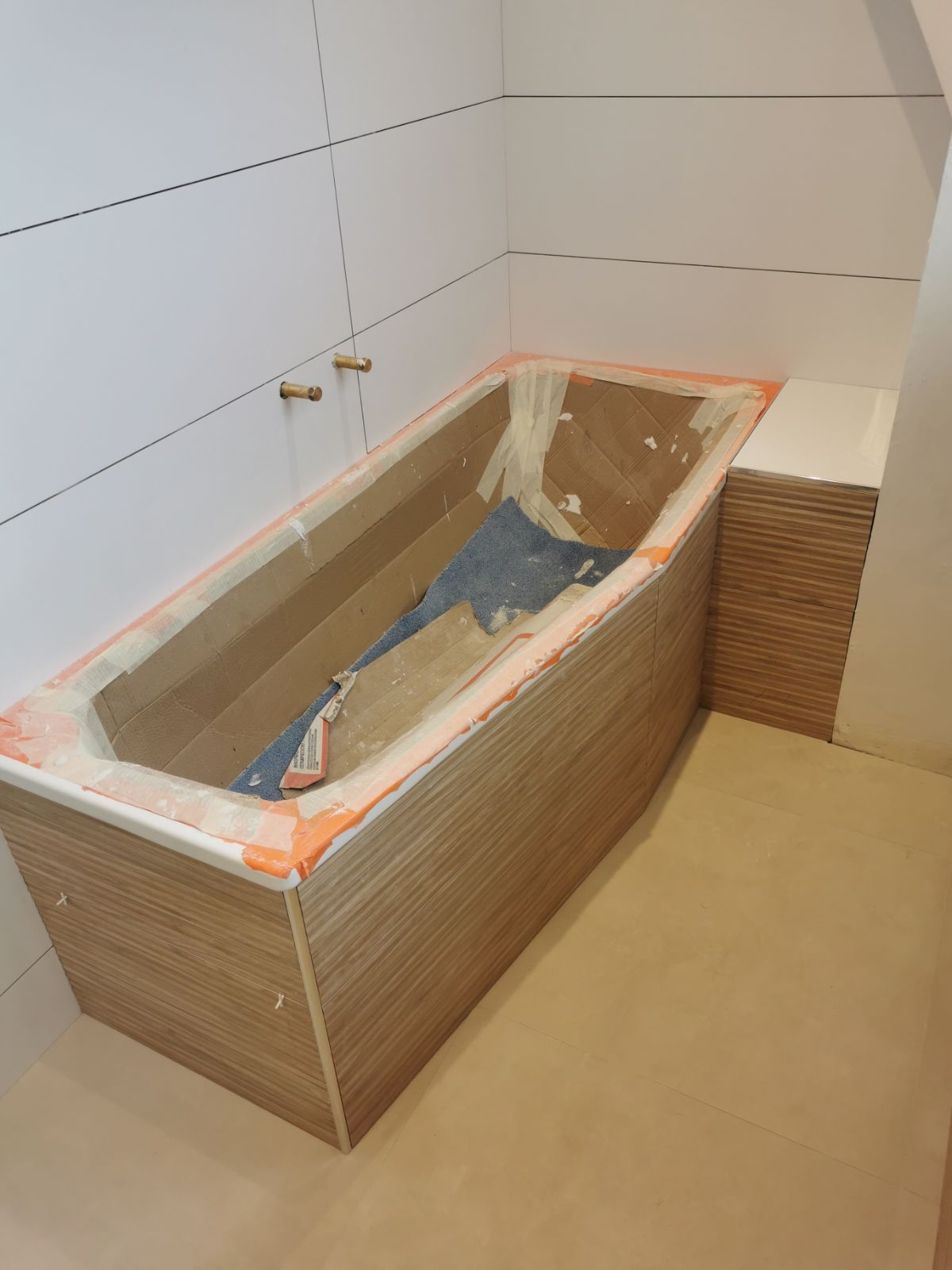 Baignoire installée avec tablier carrelé, sol revêtu et arrivée de robinetterie prête à être raccordée.